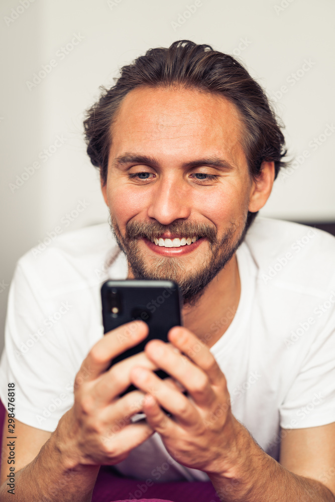 Handsome smiling young man lying on bed while holding his mobile phone. Handsome smiling young man lying on bed while holding his mobile phone.