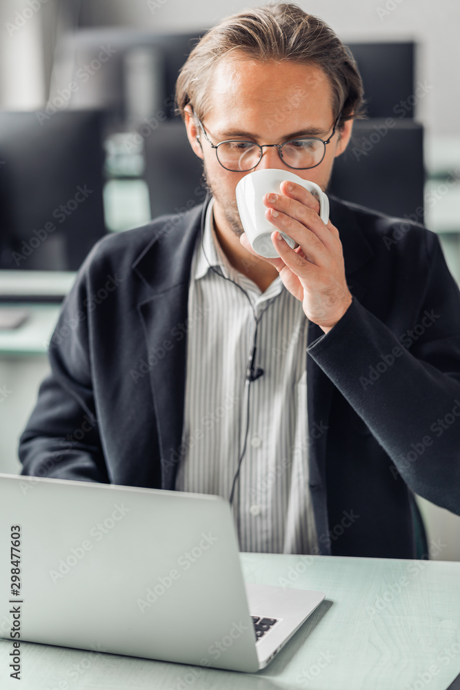 Fototapeta premium Young handsome man drinking coffee while working by the computer station.