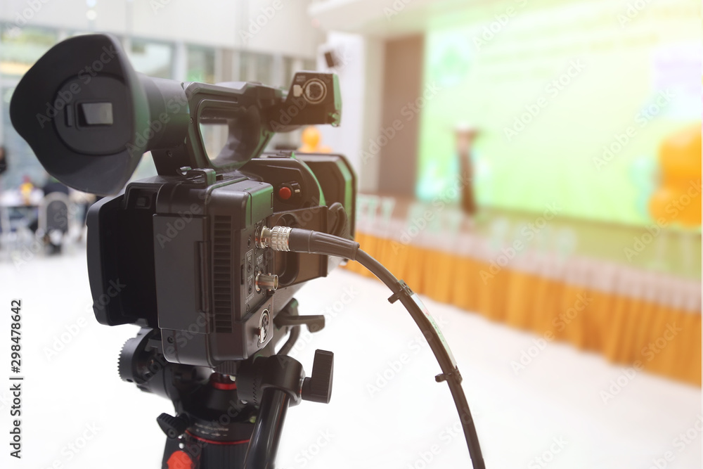 Camera filming on a tripod is broadcasting live on stage. Video camera with blurred of the stage background. Camera filming on a tripod is broadcasting live on stage. Video camera with blurred of the stage background.
