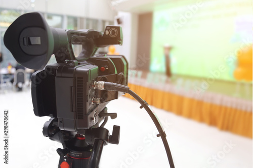 Camera filming on a tripod is broadcasting live on stage. Video camera with blurred of the stage background.