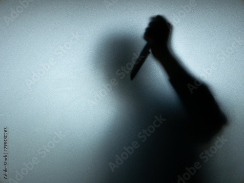 Halloween concept. Blurred shadow of hand holding sharp knife behind white mirror background. Murder scene.