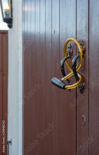 Shallow focus of a generic steel-wire bicycle antitheft device seen looped through the handles of a double door garage. Helping to deter possible entry, also in view its a lit PIR light.