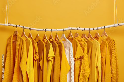 Set of bright yellow clothes and one white sweater on hangers. Collection of womens attires to wear. Variety of outfits for warm and hot weather. Wadrobe closet. Fashion, shopping and consumerism photo