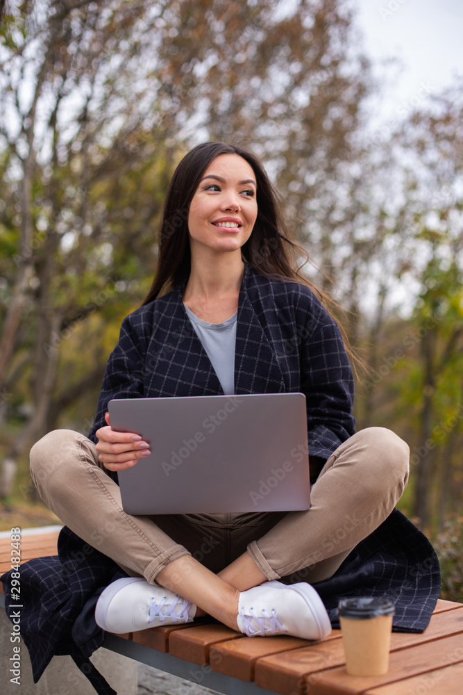 Young beautiful casual woman happily working with laptop and coffee to go in city park Young beautiful casual woman happily working with laptop and coffee to go in city park
