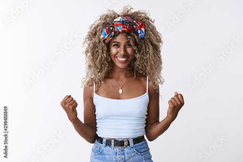 Optimistic, encouraged good-looking african american blond female with afro hairstyle, fist pump move and smiling from victory, winning lottery, celebrating amazing achievement, white background photo