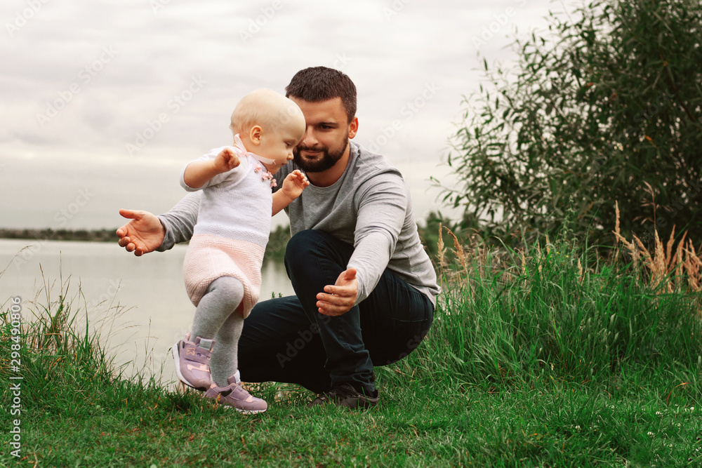 Dad teaches daughter to walk, park, nature. Walk on the grass. Father and daughter. First steps. Dad teaches daughter to walk, park, nature. Walk on the grass. Father and daughter. First steps.