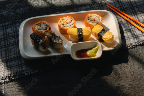 Sushi on a white plate chopsticks on the wooden table by the window in kitchen with morning sunlight, Black background and tableware, Selective focus.