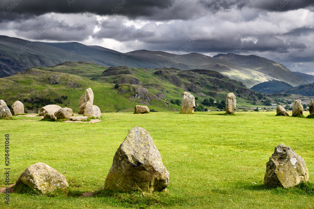Castlerigg Stone Circle under dark storm clouds on summer solstice eve with Helvellyn Range mountains Keswick Cumbria England