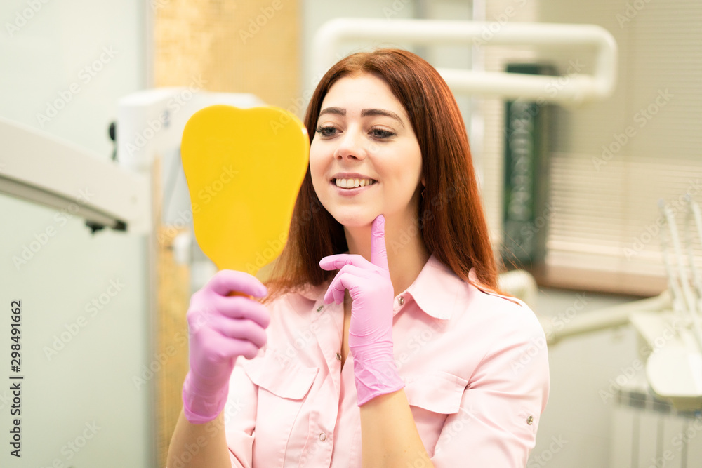 Beautiful female dentist shows healthy teeth. Smiling and holding a mirror. Dentistry and oral hygiene. Beautiful female dentist shows healthy teeth. Smiling and holding a mirror. Dentistry and oral hygiene.