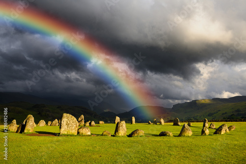 Rainbow over Castlerigg Stone Circle on summer solstice eve with sun and dark clouds over Cumbrian Mountains in Lake District Keswick England photo
