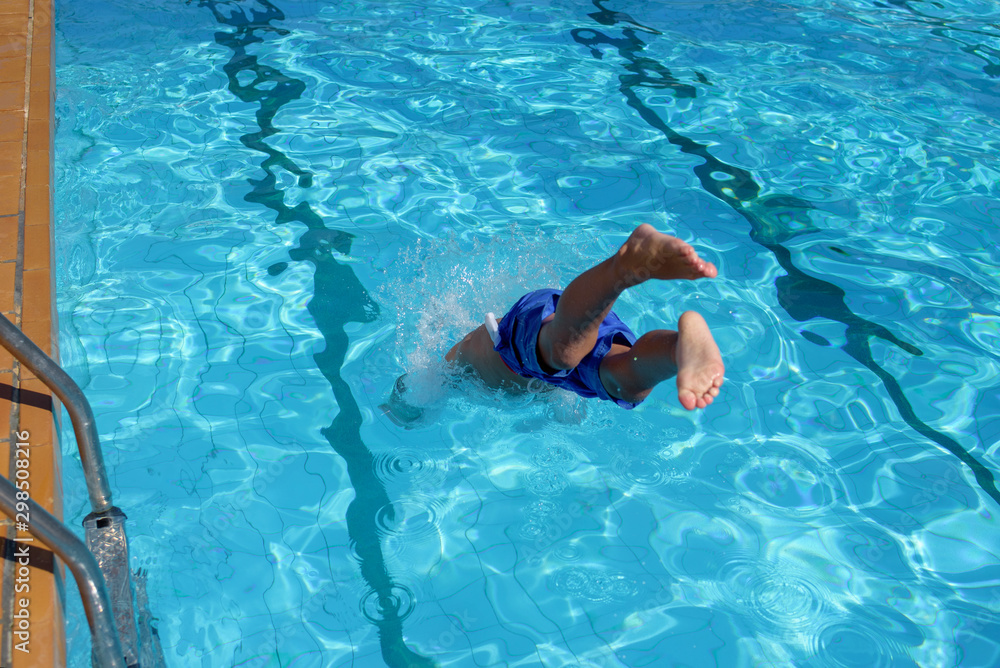 European boy  jumping into swimming pool at resort. Moment of entrance in water. His legs are stick out of water.