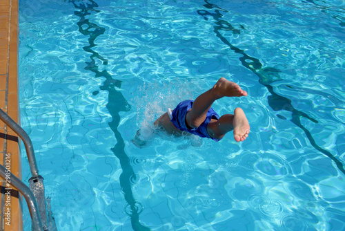 European boy jumping into swimming pool at resort. Moment of entrance in water. His legs are stick out of water.