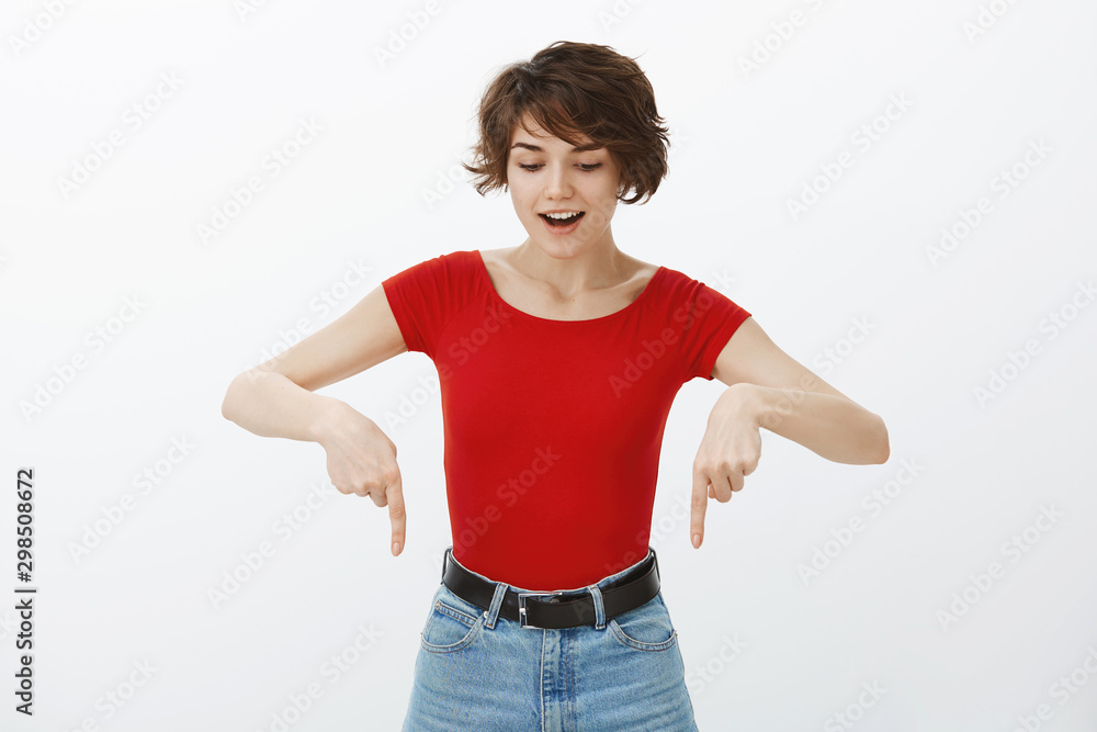 Excited good-looking european female short pixie haircut look pointing down amazed entertained curiously contemplating amused indicating bottom promo smilling broadly astonished white background Excited good-looking european female short pixie haircut look pointing down amazed entertained curiously contemplating amused indicating bottom promo smilling broadly astonished white background