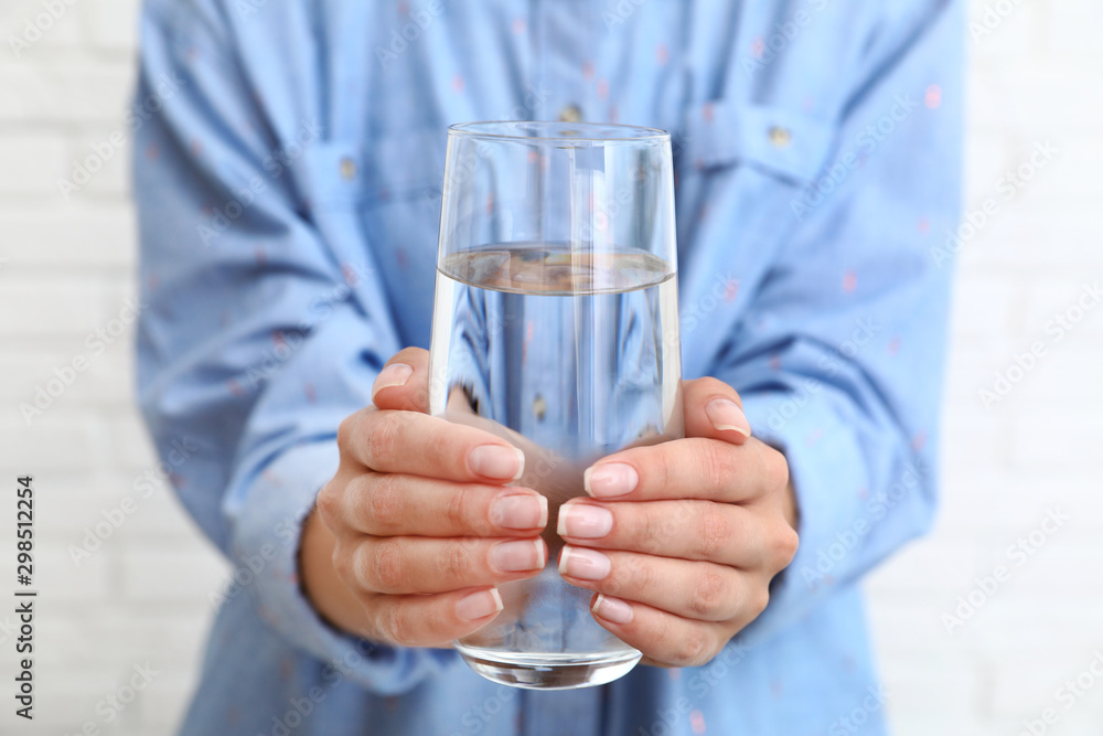 Woman holding glass of water near brick wall, closeup. Refreshing drink Woman holding glass of water near brick wall, closeup. Refreshing drink