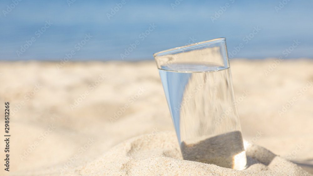 Sandy beach with glass of refreshing drink on hot summer day, space for text Sandy beach with glass of refreshing drink on hot summer day, space for text