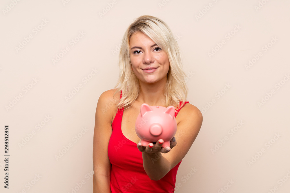 Young blonde woman over isolated background holding a big piggybank Young blonde woman over isolated background holding a big piggybank