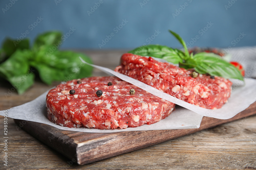 Raw meat cutlets for burger on wooden table against blue background, closeup Raw meat cutlets for burger on wooden table against blue background, closeup