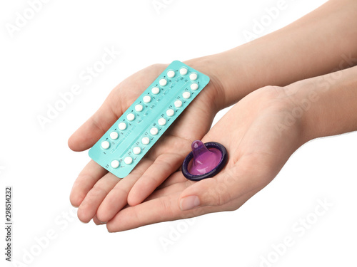 Young woman holding birth control pills and condom on white background, closeup. Safe sex concept