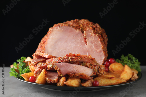 Plate with delicious ham and potatoes on grey table against black background