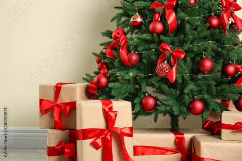 Fotografia Decorated Christmas tree and gift boxes near beige wall