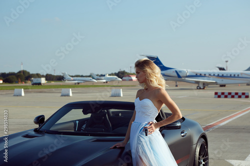 The elegant blonde beautiful woman posing near luxury vehicle on planes background. Girl wearing blue dress. No retouch. © sarymsakov.com