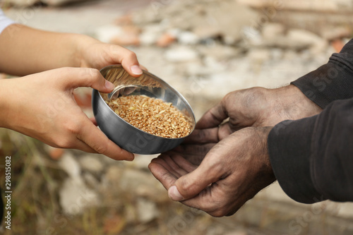 Woman giving poor homeless man bowl of wheat outdoors, closeup