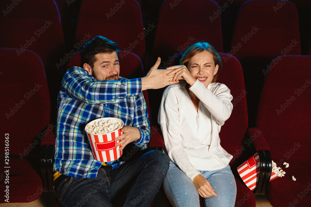 Naklejka premium Attractive young caucasian couple watching a film at a movie theater, house or cinema. Look expressive, astonished and emotional. Sitting alone and having fun. Relation, love, family, weekend time.