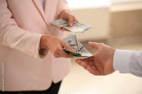 Businesswoman giving dollar bills to man on blurred background, closeup