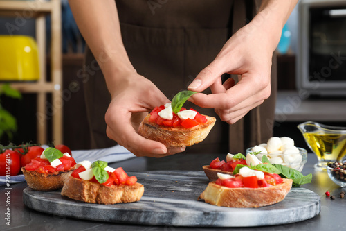 Woman preparing delicious bruschettas with cheese and tomatoes at table, closeup