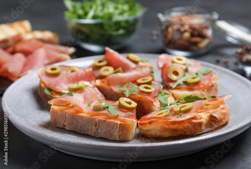 Delicious bruschettas with prosciutto and olives on table, closeup