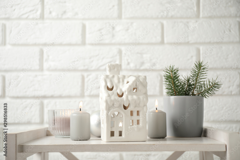 Composition with house shaped candle holder on white wooden table near brick wall. Christmas decoration Composition with house shaped candle holder on white wooden table near brick wall. Christmas decoration