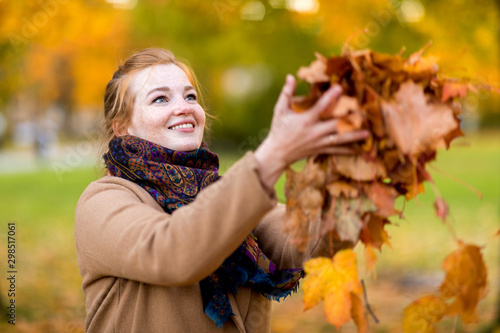 Girl in a camel coat in autumn park smiles and catches falling leaves