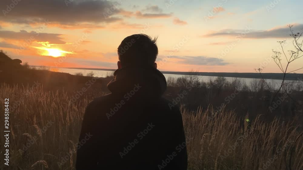 The man enjoys the sunset. Dreaming guy stands against the background of sunset and hope for a good future. Stress relief peace of mind. Concept relax. Silhouette of a young man on background of sea The man enjoys the sunset. Dreaming guy stands against the background of sunset and hope for a good future. Stress relief peace of mind. Concept relax. Silhouette of a young man on background of sea