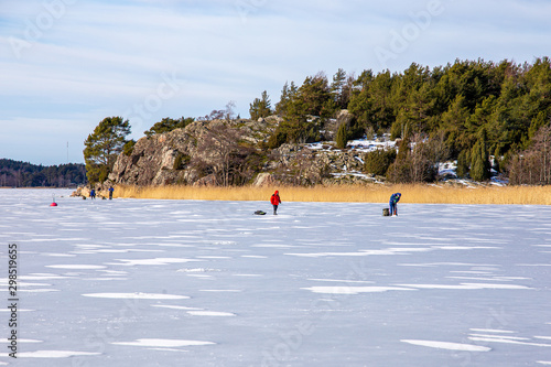 Ice skating and fishing over the frozen baltic sea in Naantali, Finland. Sunny winter day with bright blue sky.