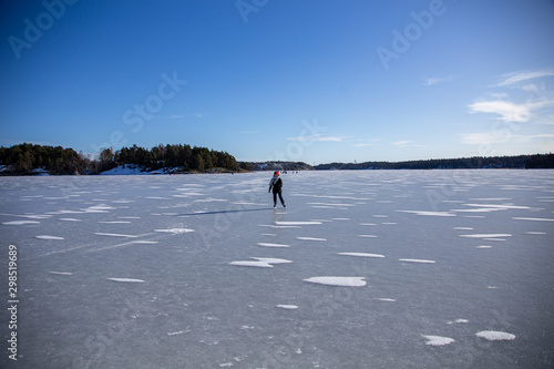 Ice skating and fishing over the frozen baltic sea in Naantali, Finland. Sunny winter day with bright blue sky.