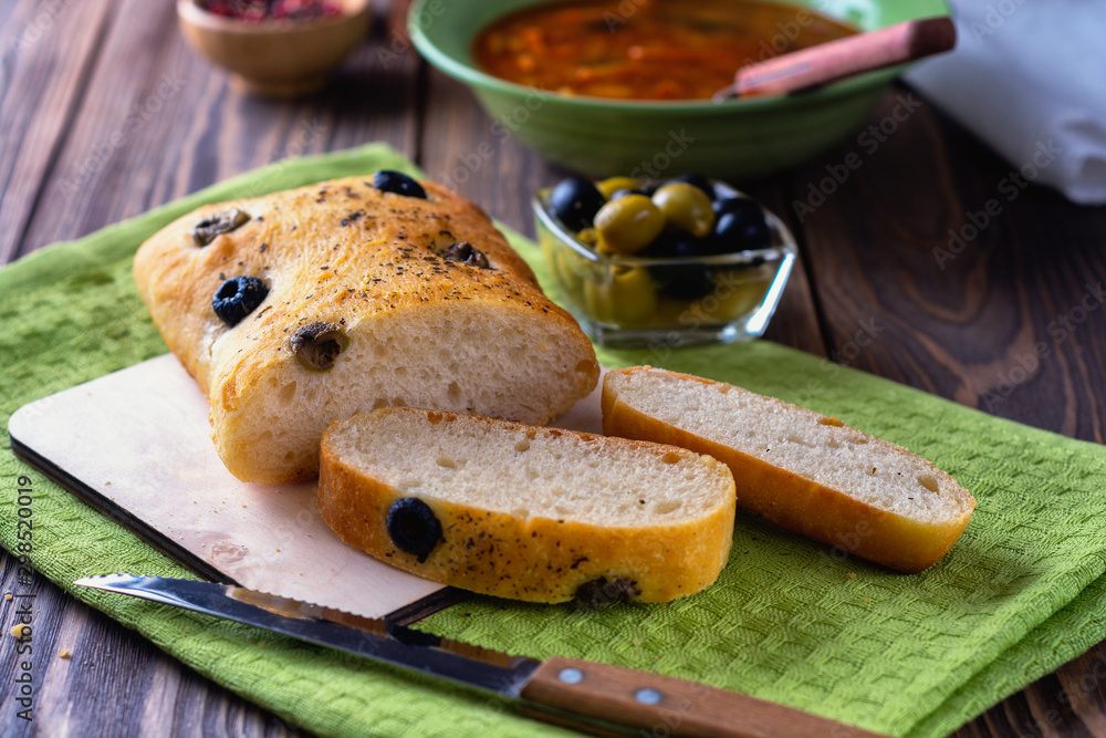 Fresh italian ciabatta bread with olives on a linen napkin next to plates on a wooden table