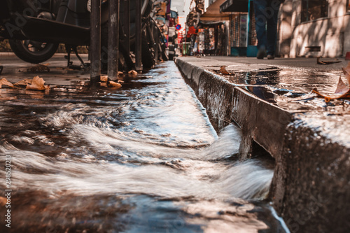 Quadro em tela Stormy water on the sidewalk in a strong stream through curbs and in storm chann