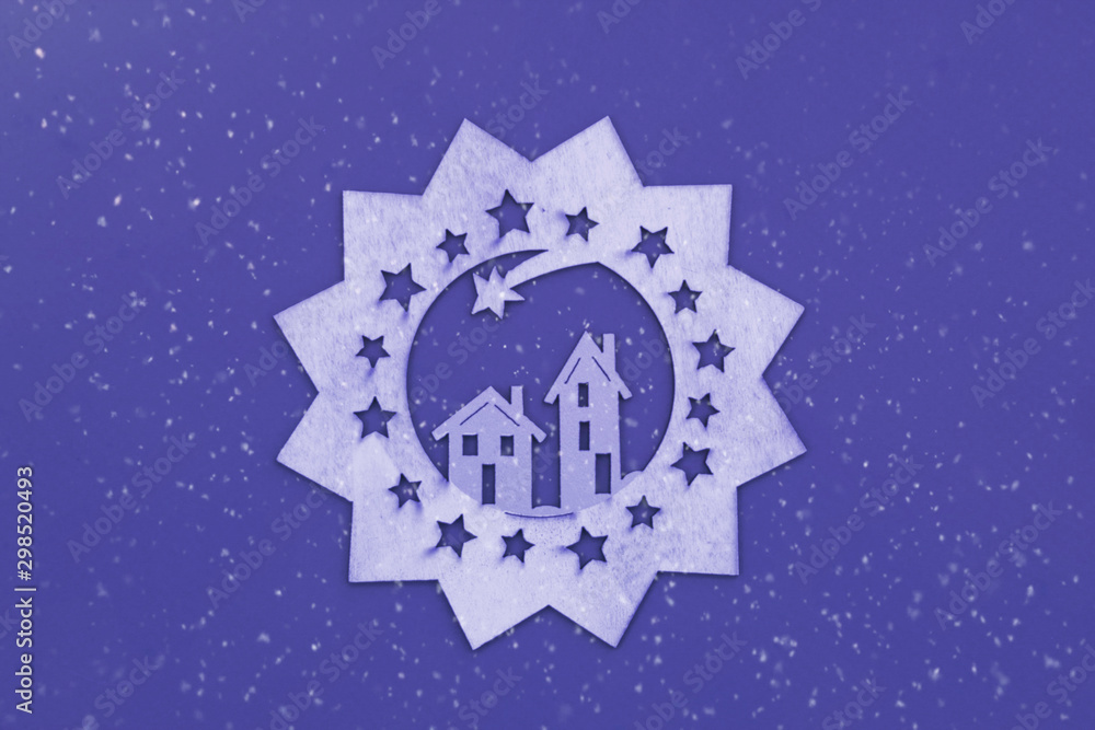 Christmas drawing with houses and a shooting star cut from a wooden sheet on a purple background with snow.