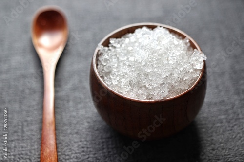 dead sea salt in bamboo bowl with wooden spoon on dark gray background closeup
