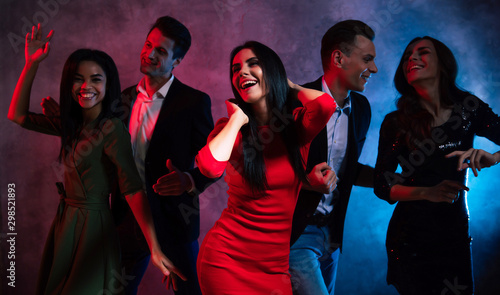 Young and gracious. A pleasant company of five well-dressed multicultural friends is dancing in the dark, expressing extreme joy and contentment with their party.
