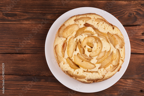 Baked apple pie in a white plate on a brown wooden background with copy-space