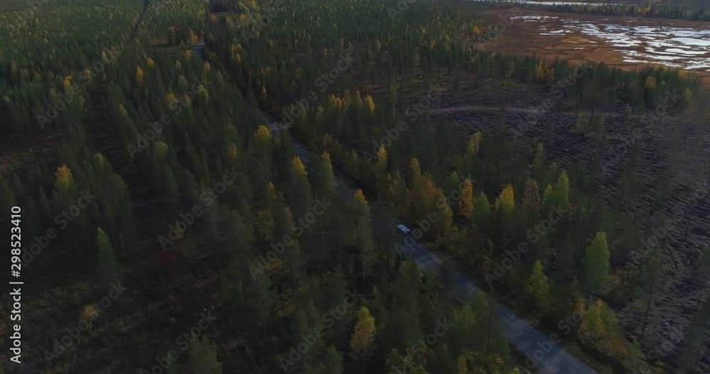 Camper on a forest road, Aerial, tilt up, drone shot, of a camper van, driving on a route, between foliage trees and swamps, fells in the background, sunny day, in Pyha-Luosto national park, Finland Camper on a forest road, Aerial, tilt up, drone shot, of a camper van, driving on a route, between foliage trees and swamps, fells in the background, sunny day, in Pyha-Luosto national park, Finland
