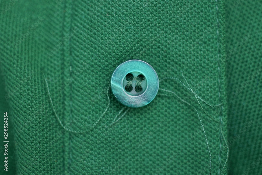one plastic button with threads on a green cloth one plastic button with threads on a green cloth