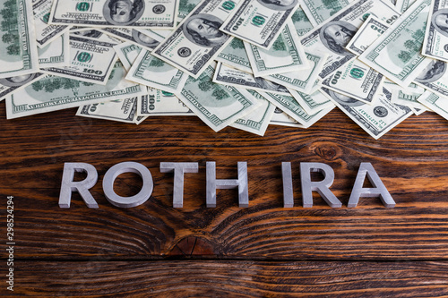 words ROTH IRA laid on wooden surface by metal letters with us dollar banknotes