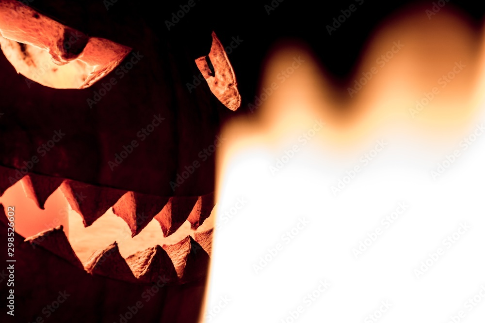 Fototapeta premium Carved spooky halloween pumpkin in hot burning hell fire flames. Big helloween autumn symbol with mad face, glowing eyes, mouth and teeth. Scary hot nightmare horror with evil smile at october 31st
