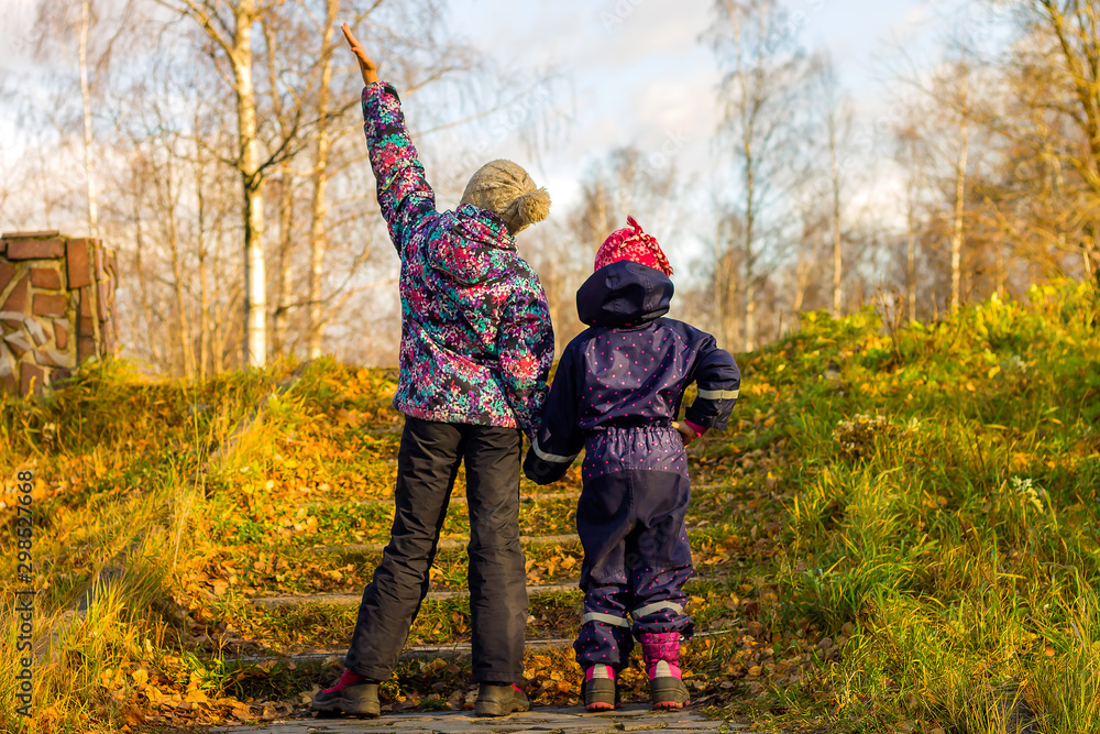 Two sisters stand with their backs on the old park stairs,the eldest holds the younger by the hand and explains something Two sisters stand with their backs on the old park stairs,the eldest holds the younger by the hand and explains something