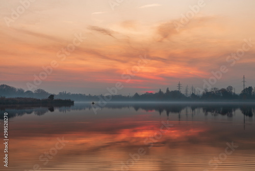 Beautiful sunset on the lake. A fisherman on a boat is fishing. Misty evening on the lake at sunset. Beautiful landscape with sunset and lake