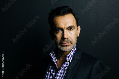 Portrait of a serious man in checkered shirt and jacket, isolated on black studio background © Carlos David