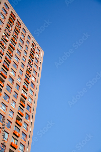 Architectural background of a fragment of orange modern residential building against the clear blue sky © Annuitti