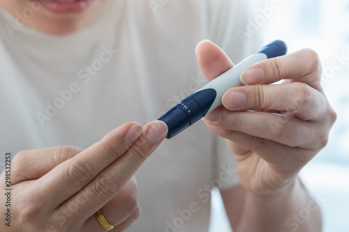 Close up of man hands using lancet on finger to check blood sugar level by Glucose meter in the morning. Use as Medicine  diabetes  glycemia  health care and people concept.